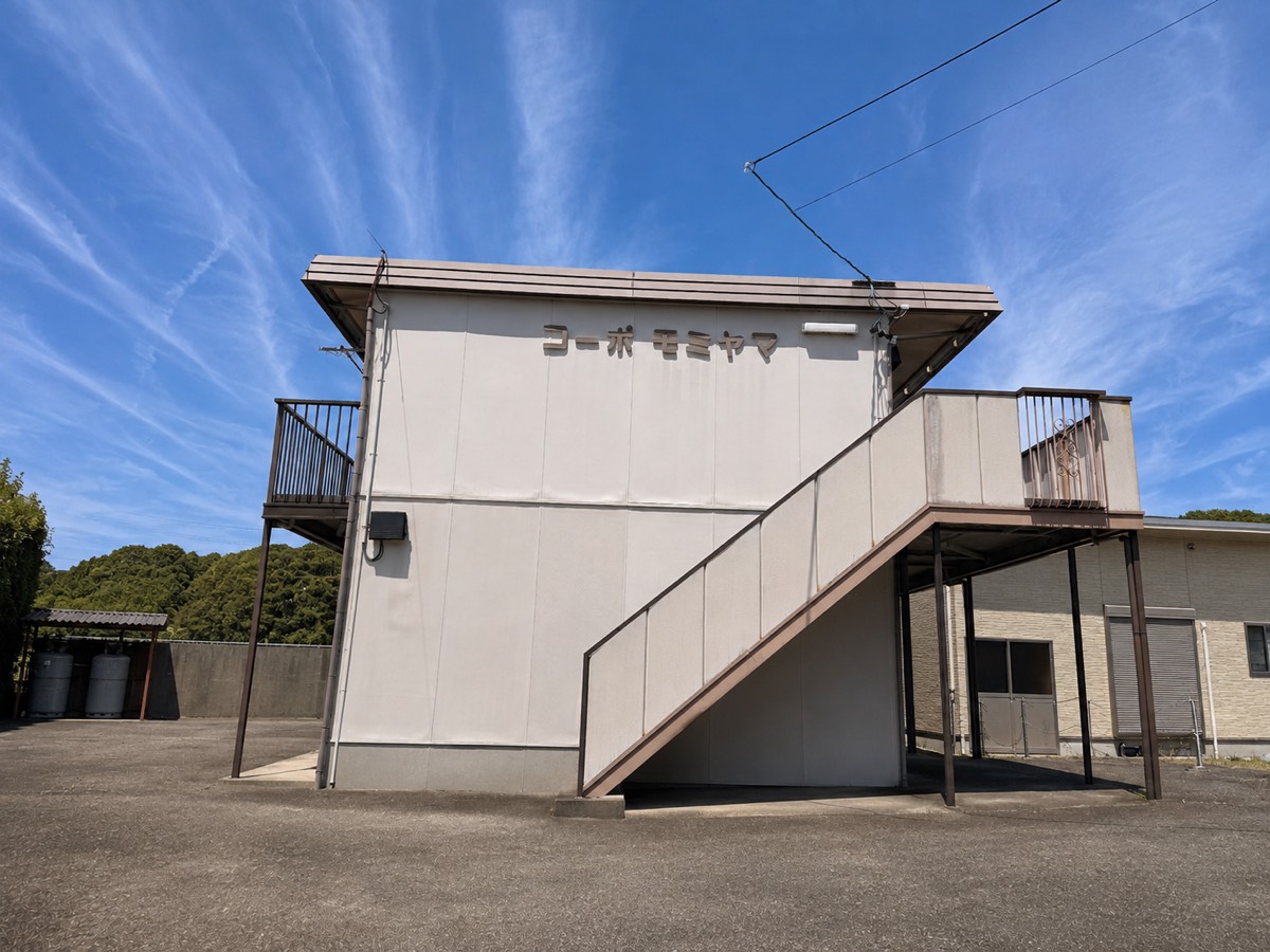 コーポモミヤマの外観。建物名の看板と外階段、手前に駐車スペース